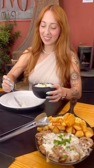 Lara, de cabelos ruivos, sorrindo enquanto experimenta uma refeição em um restaurante